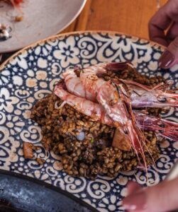 Arroz cremoso cocinado con gambas rojas y verduras y presentado en plato de cerámica