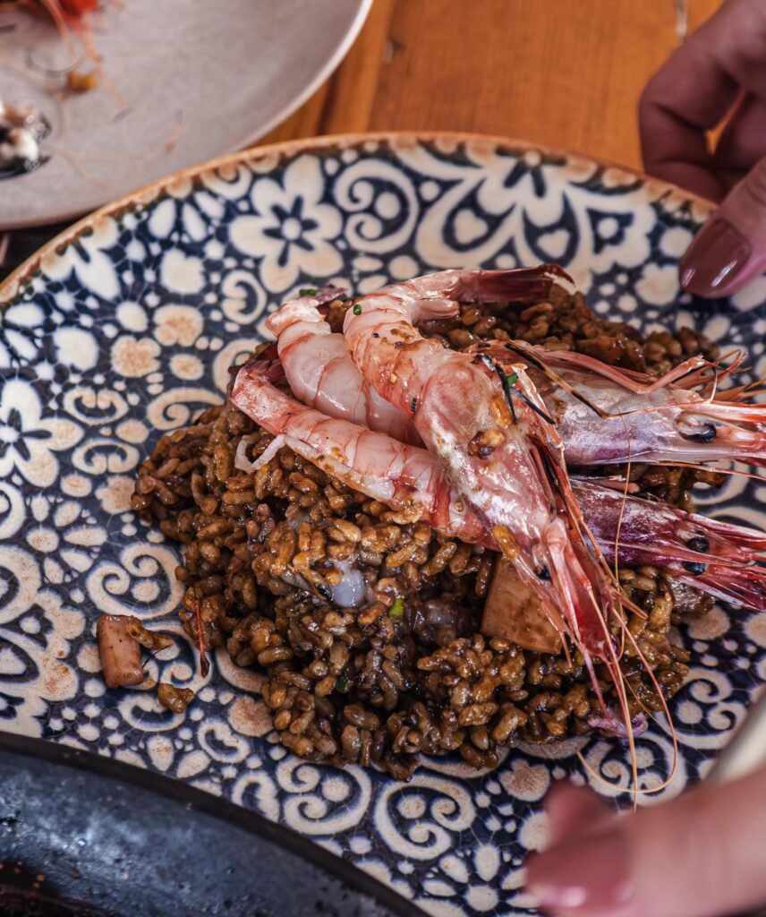 Arroz cremoso cocinado con gambas rojas y verduras y presentado en plato de cerámica
