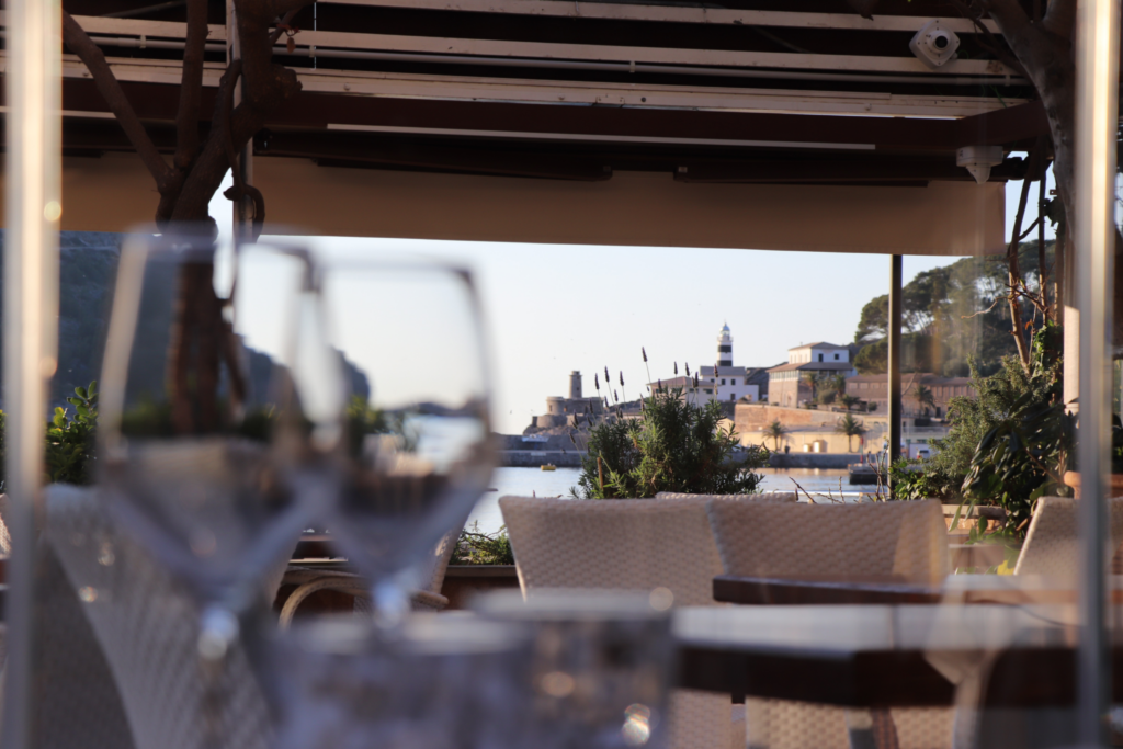 La imagen lo dice todo: una terraza abierta al Port de Sóller, copas preparadas, luz dorada cayendo sobre el mar y, al fondo, el faro